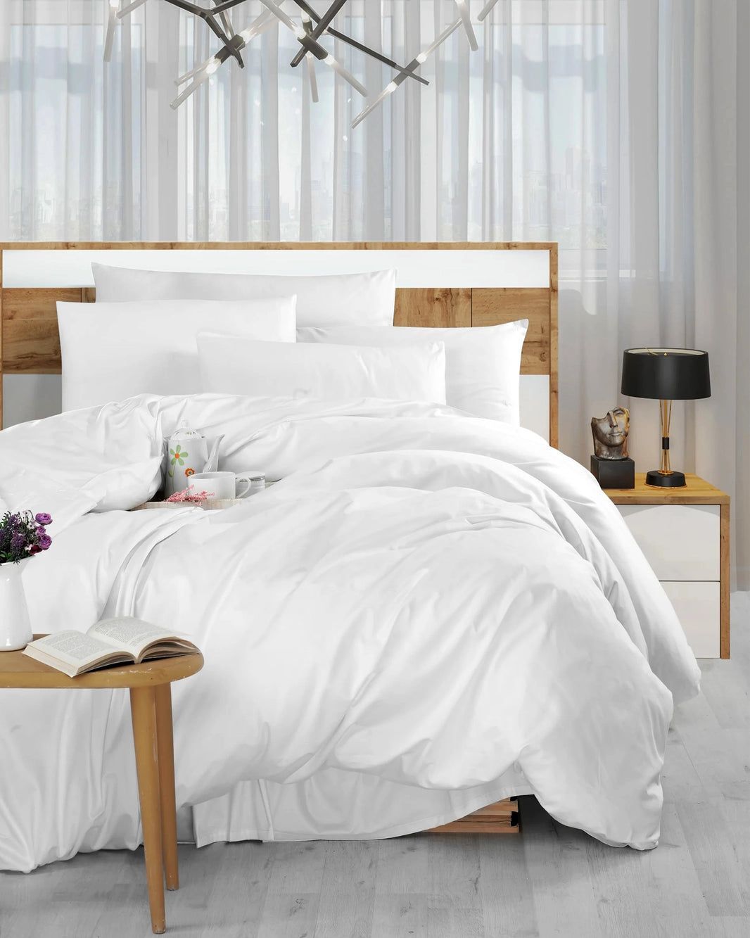 Bright white bedroom with a neatly made bed, wooden nightstand, black lamp, and sheer curtains