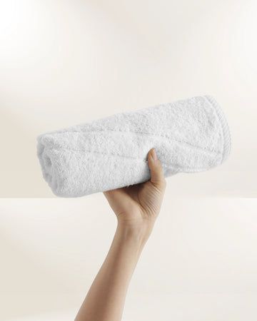 Hand holding a rolled white towel against a plain light background