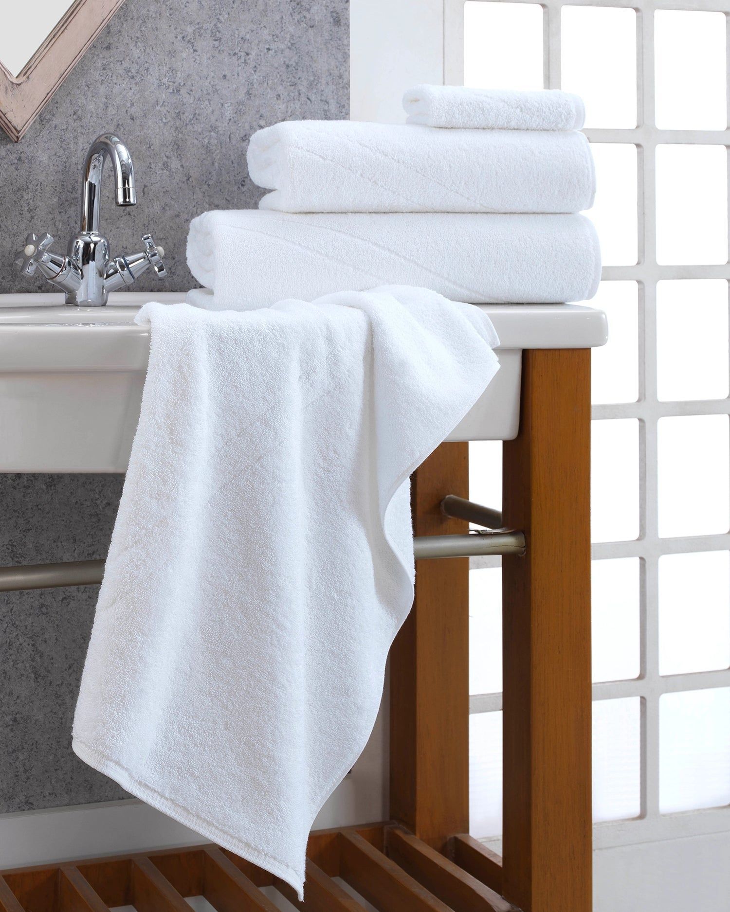 Stacked white towels on a wooden bathroom rack beside a sink