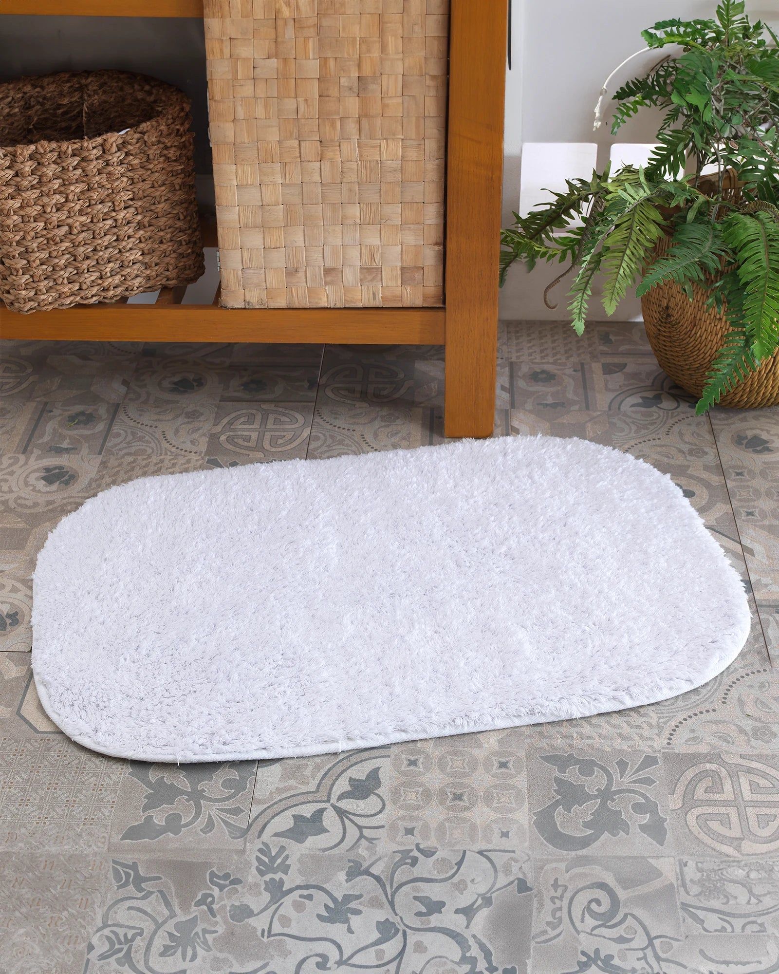 White oval rug on patterned tile floor beside a wooden cabinet and potted plant.