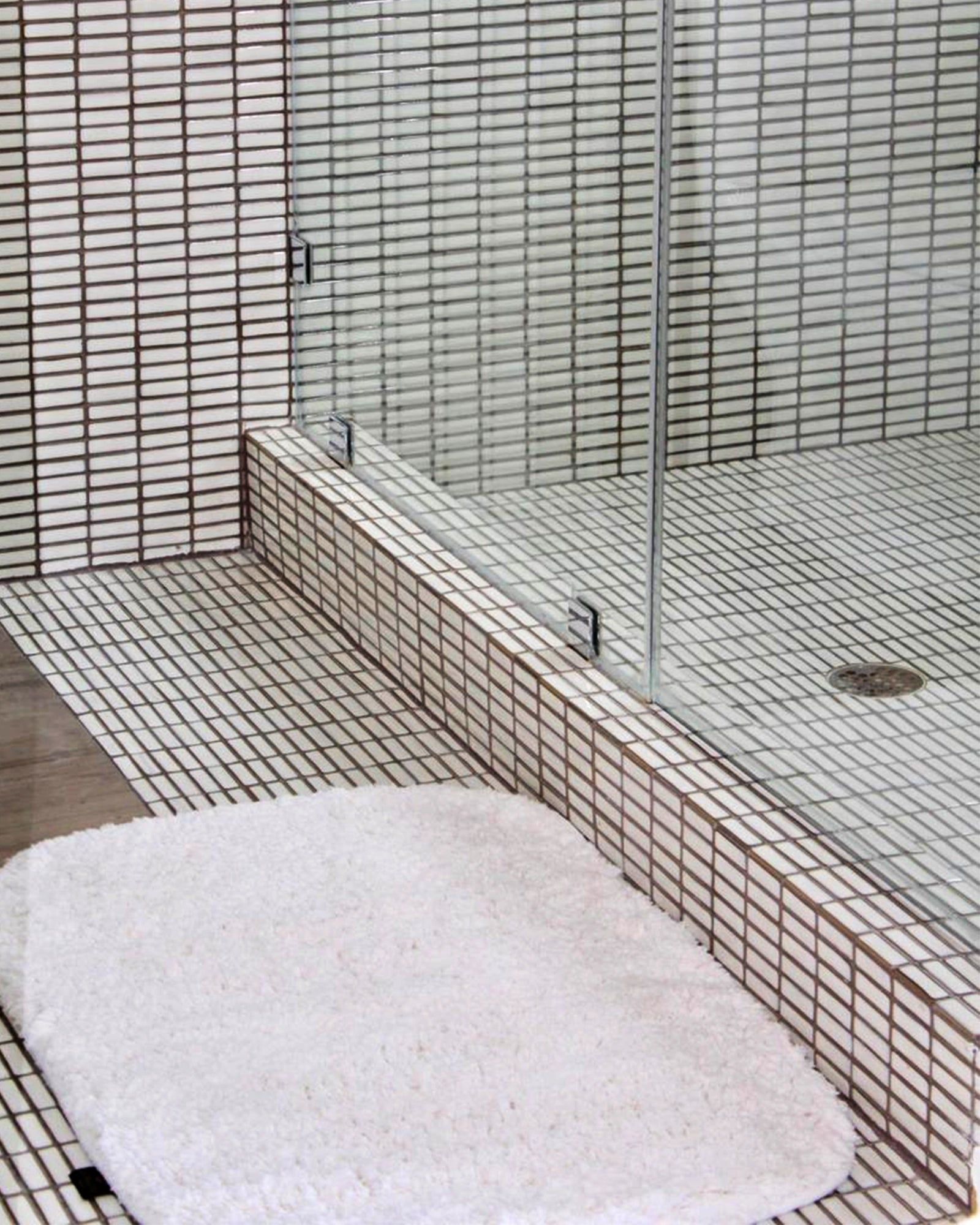 Small tiled shower area with a white seat and glass partition.