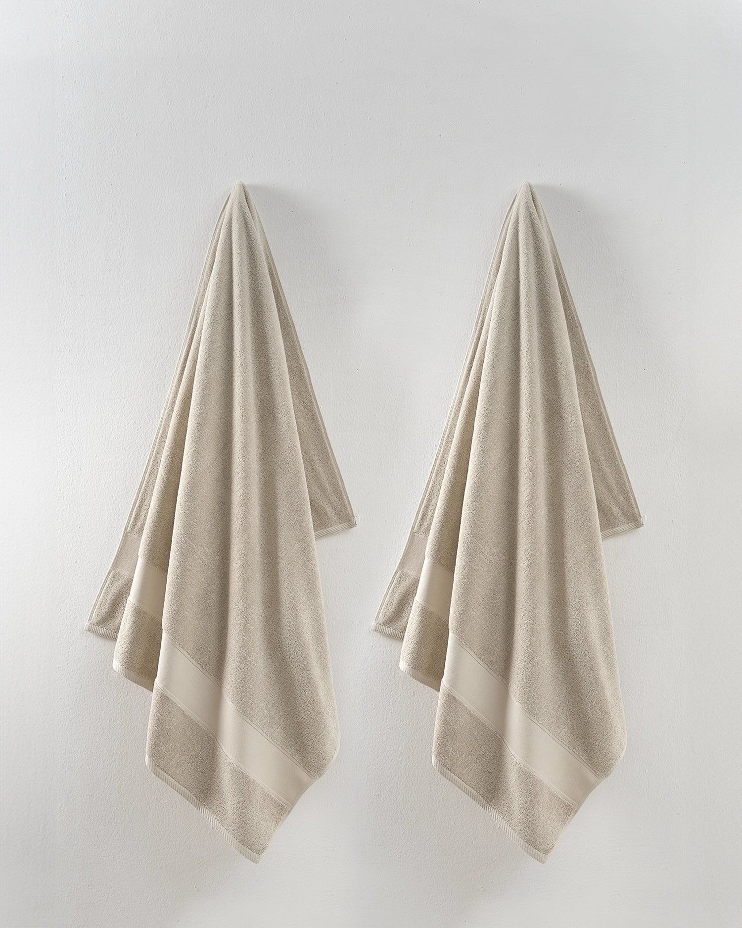 Two beige towels hanging side by side on a light wall.