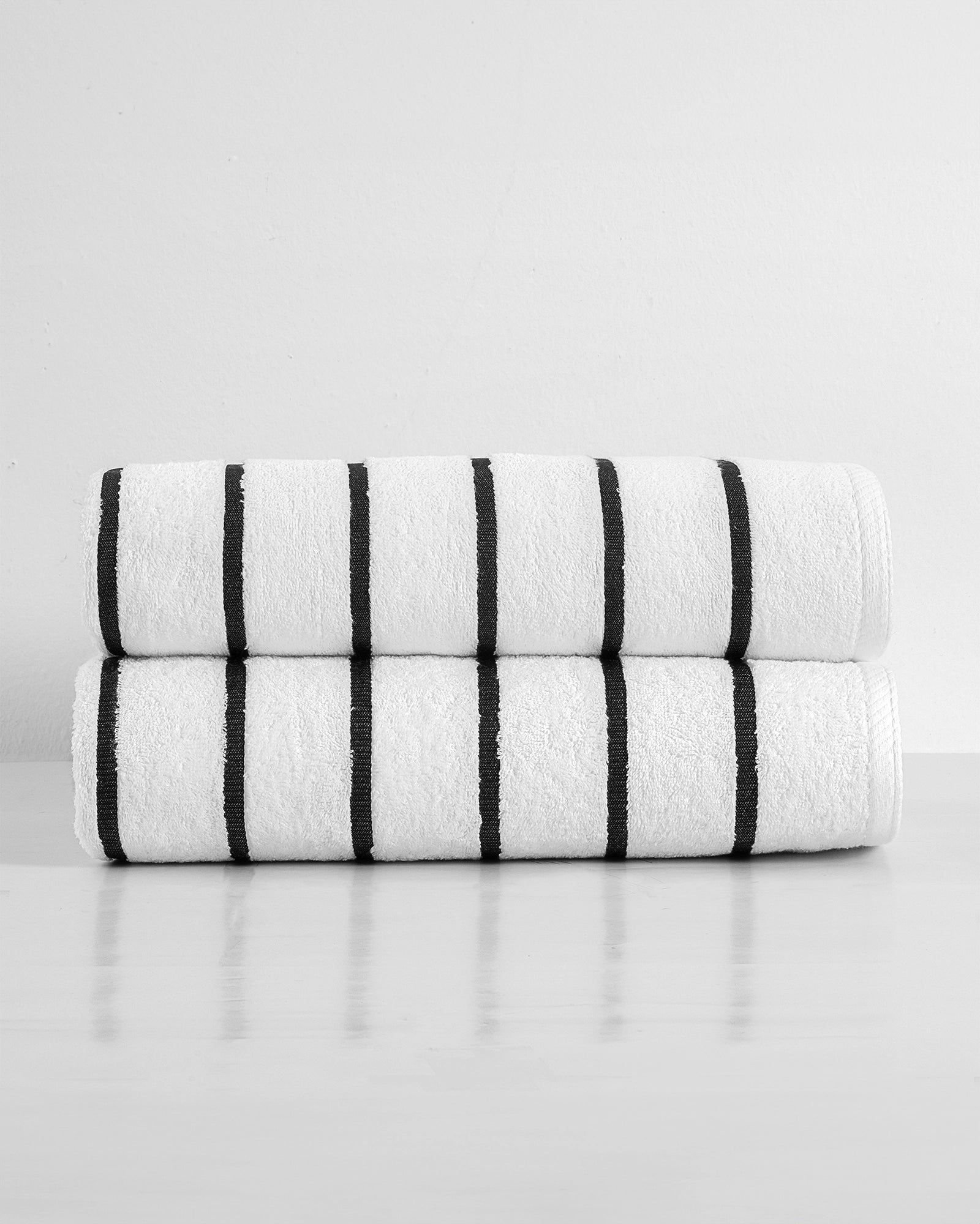 Stacked white rolled towels with black stripes on a light surface