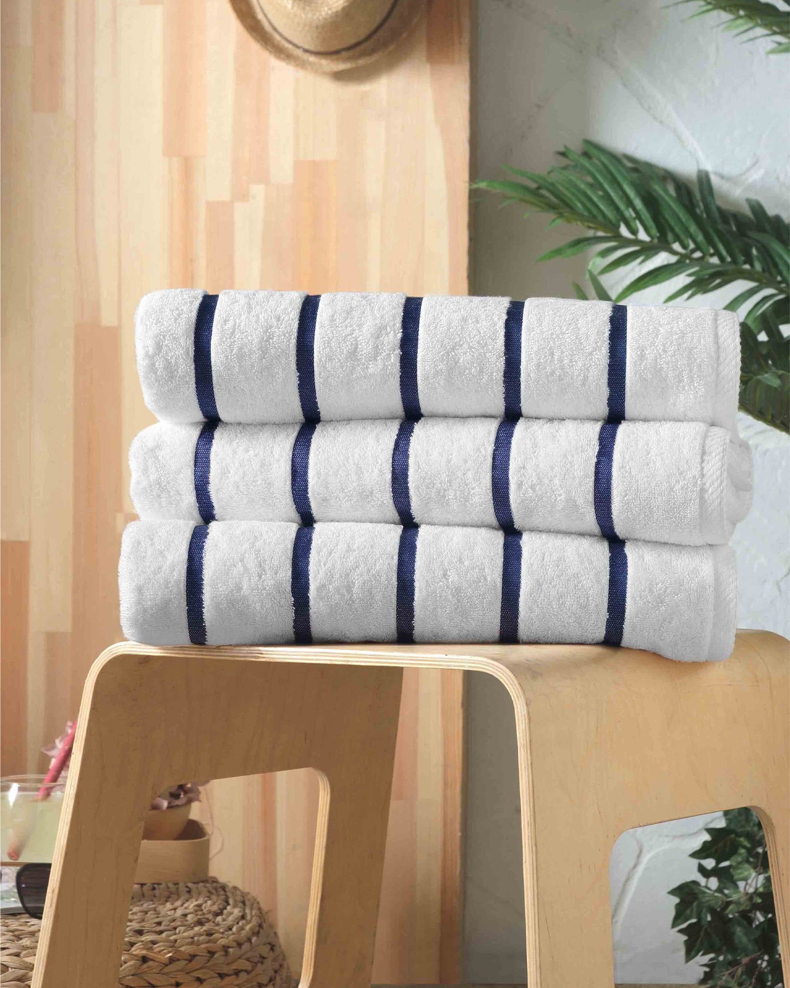 Stacked white towels with navy stripes on a wooden stool in a bright room