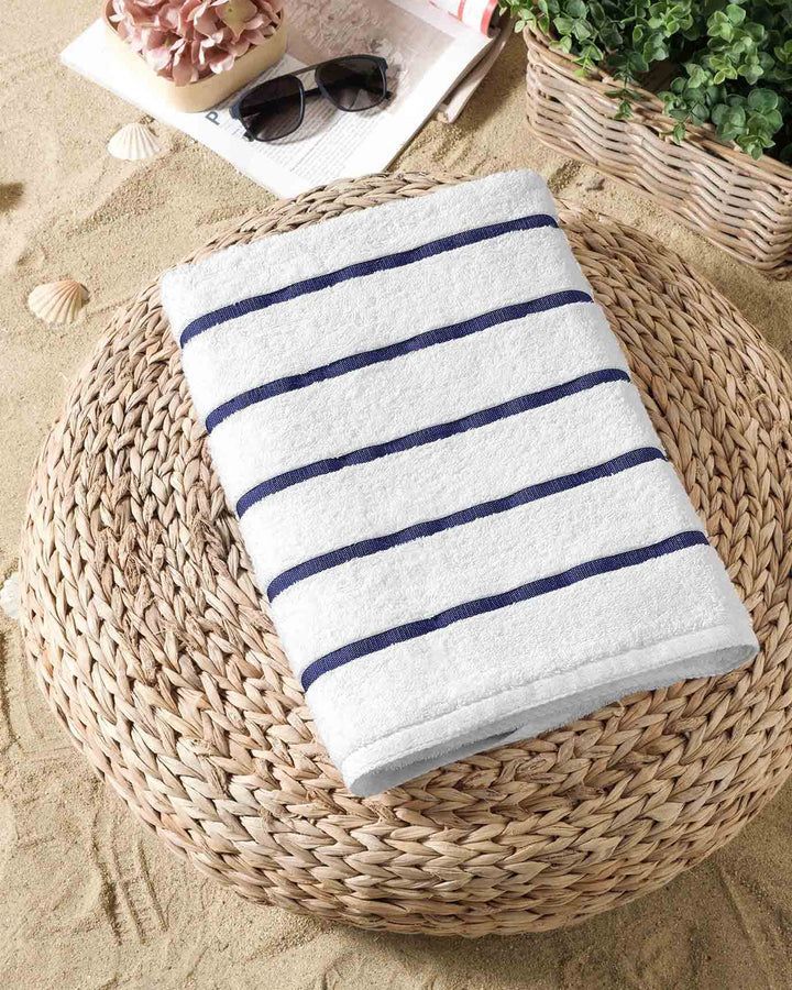 Folded white towel with navy stripes on a woven chair, beside sunglasses and a plant.