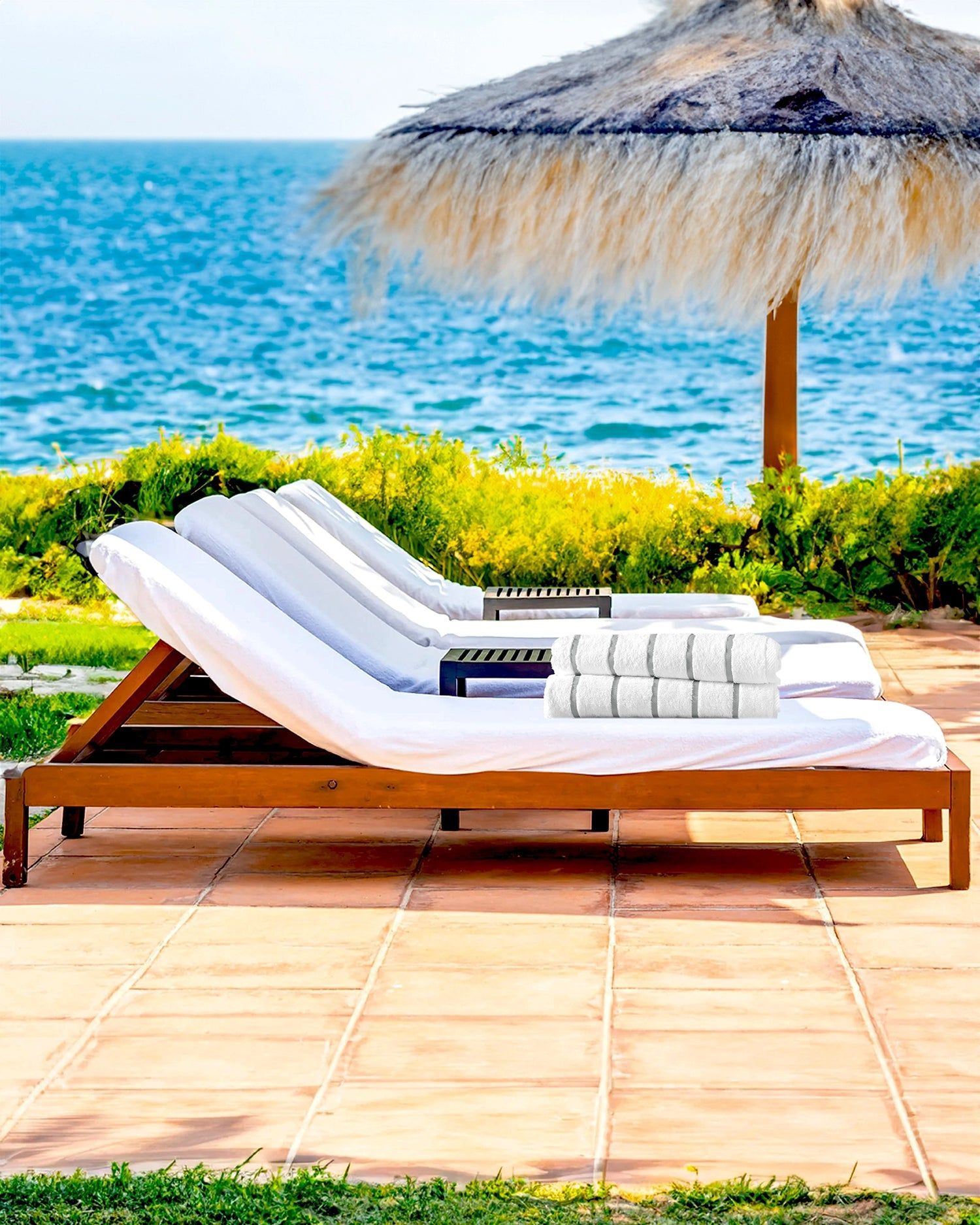 Lounge chair with white towels on a sunny patio by the ocean and a thatched umbrella