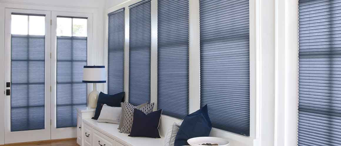 Bright sunroom with white benches, blue pillows, and tall blue patterned window shades