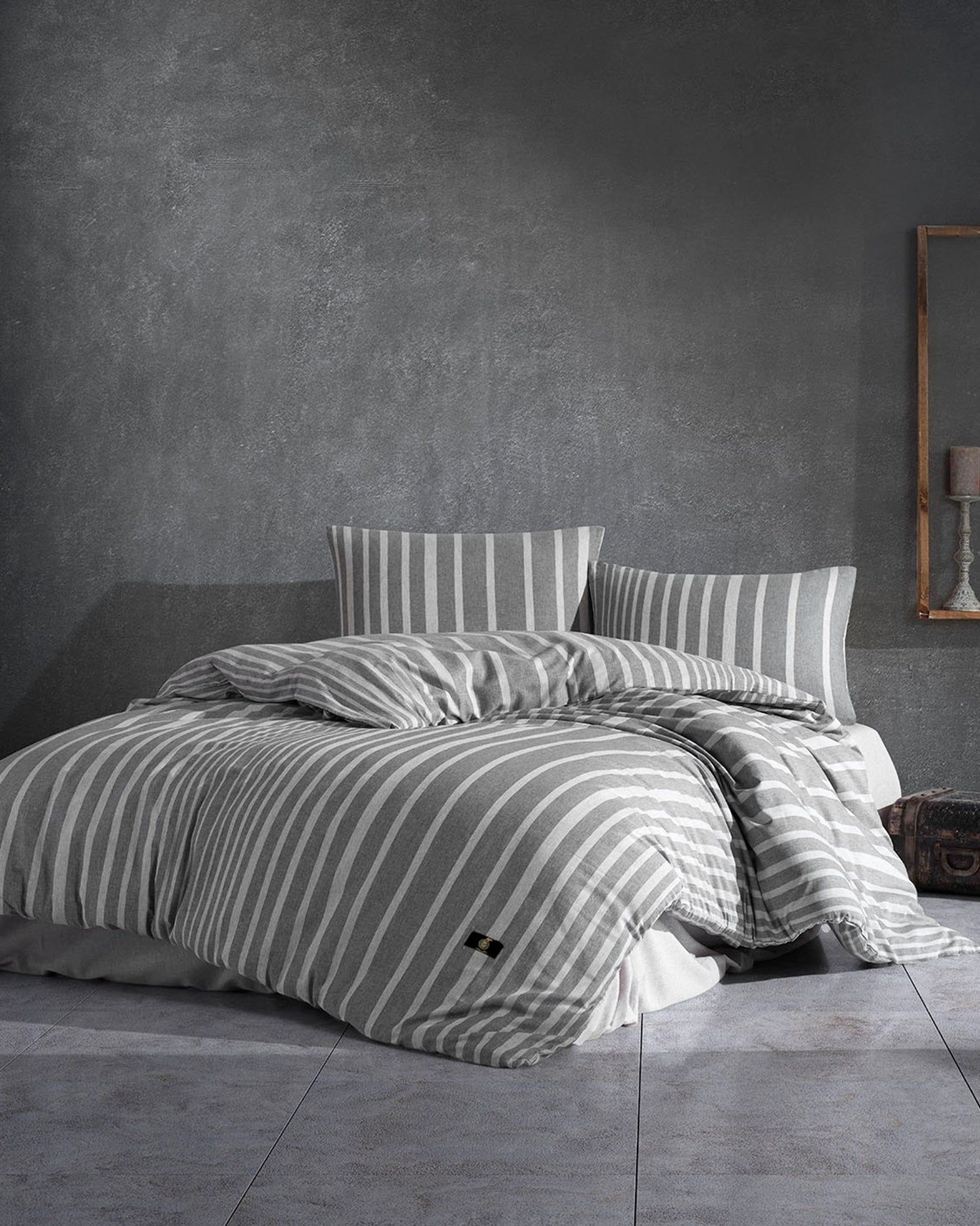 Striped bedding on an unmade bed in a minimalist gray bedroom, with striped pillows and a textured wall.