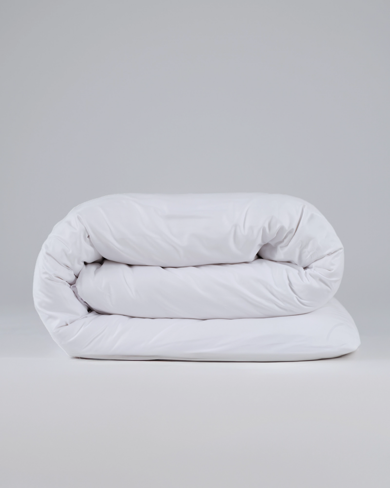 Folded white comforter or duvet on a plain light gray background