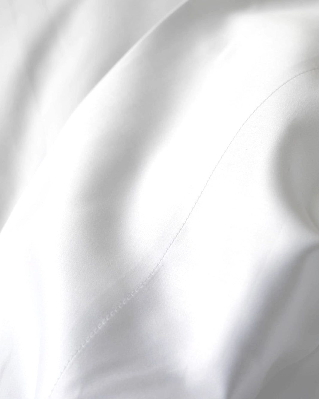 Close-up of white satin fabric with soft folds and stitching detail