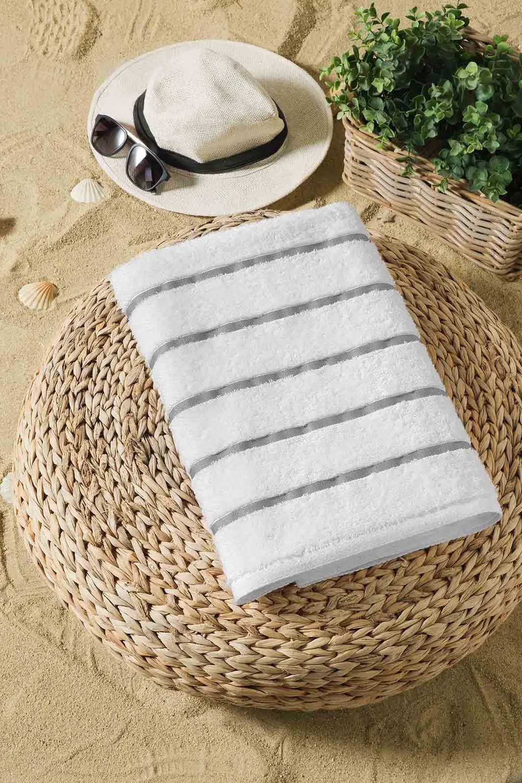 Folded white striped towel on a woven chair beside a hat, sunglasses, and greenery.