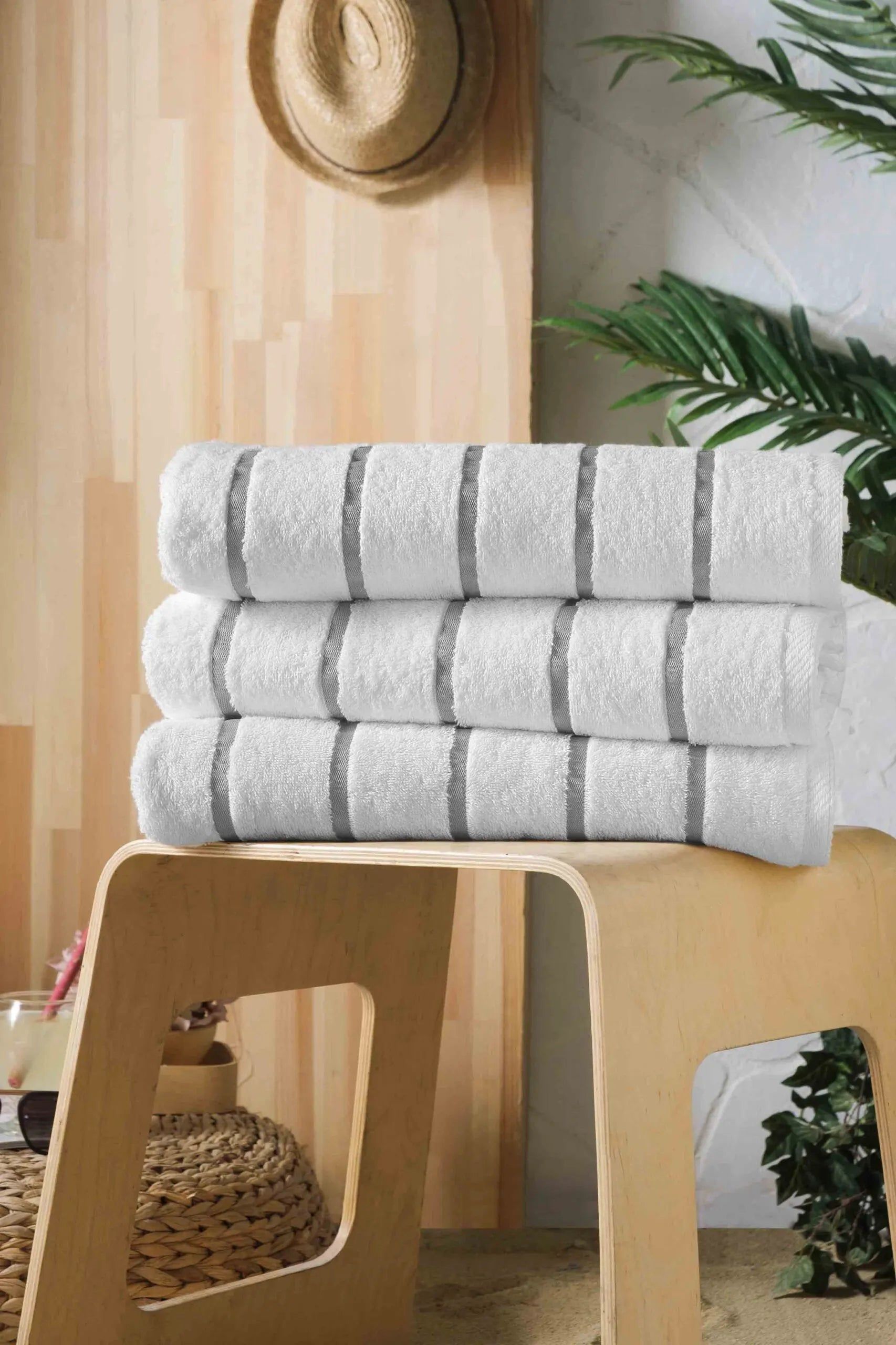 Stack of folded white towels on a wooden stool in a bright, plant-filled room