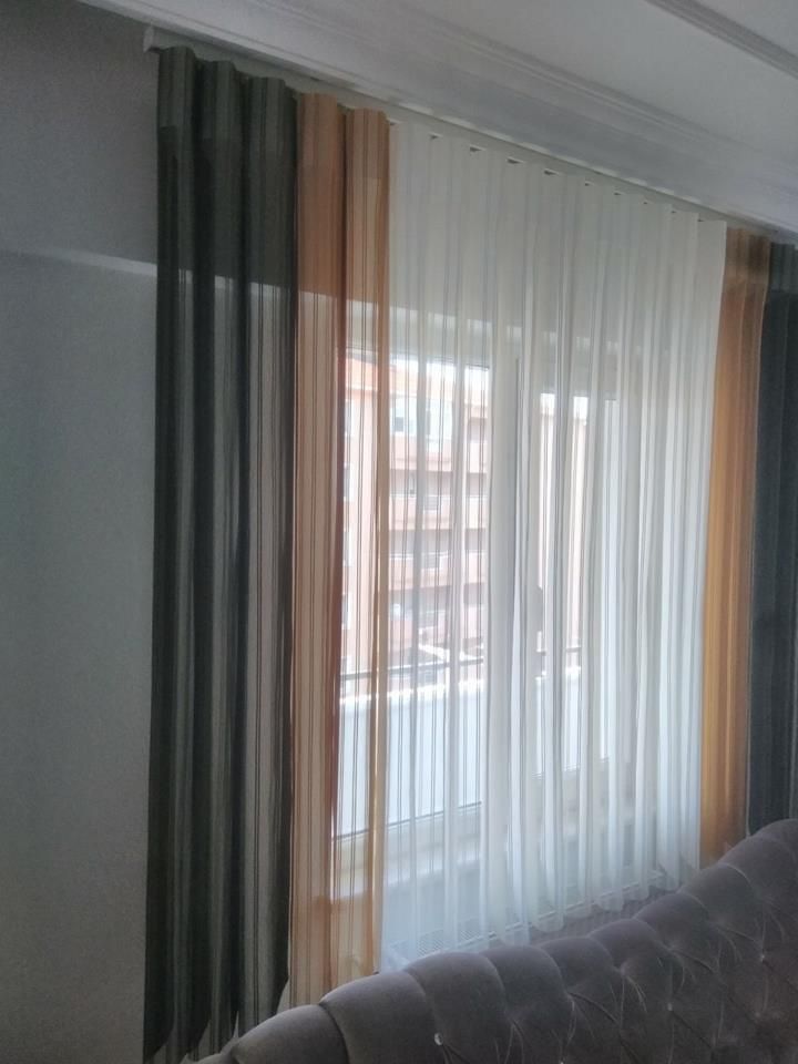 Sheer white curtains with dark drapes beside a window, with a gray tufted sofa in the foreground