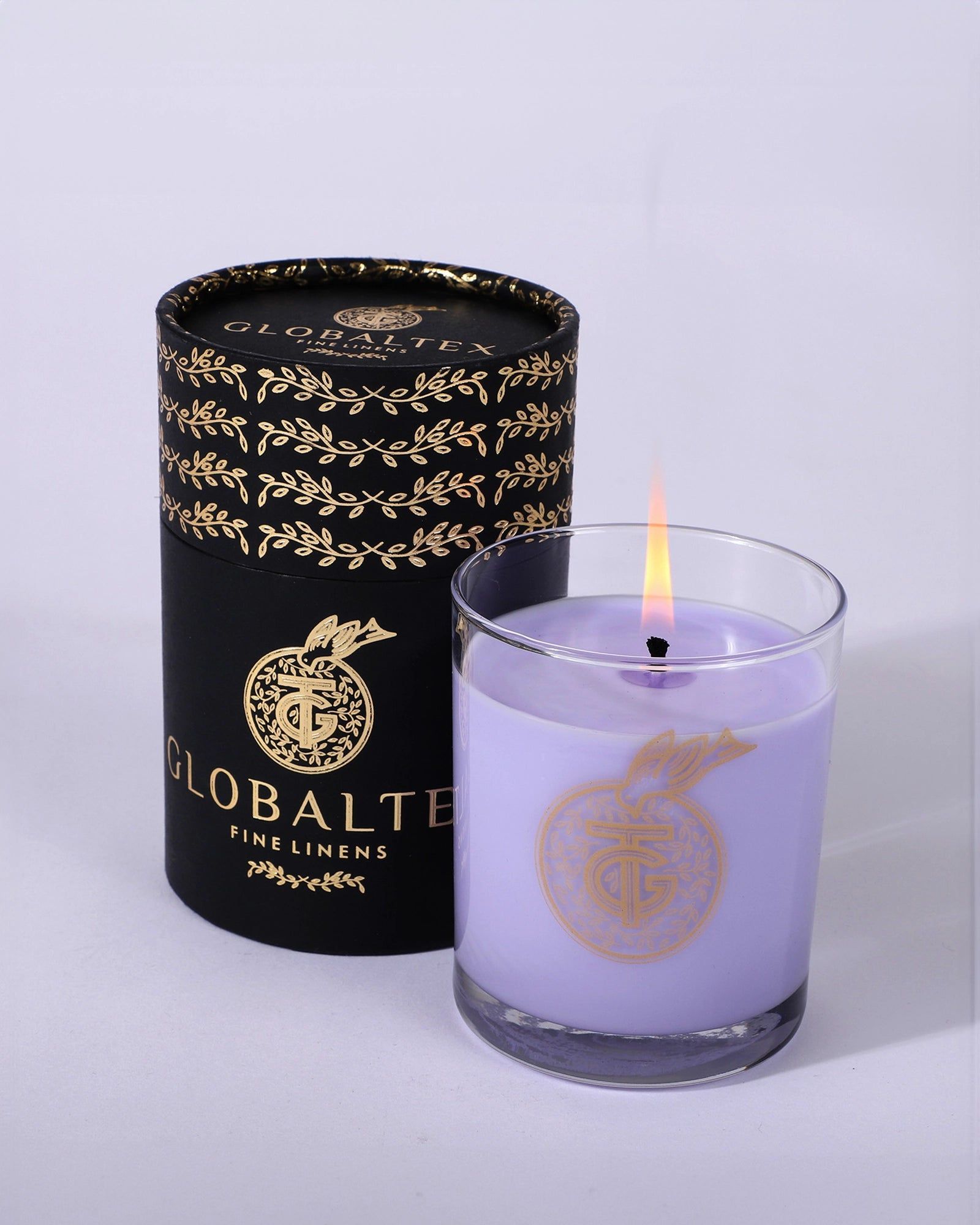 Black candle tin and lit lavender candle jar with gold branding on a light background