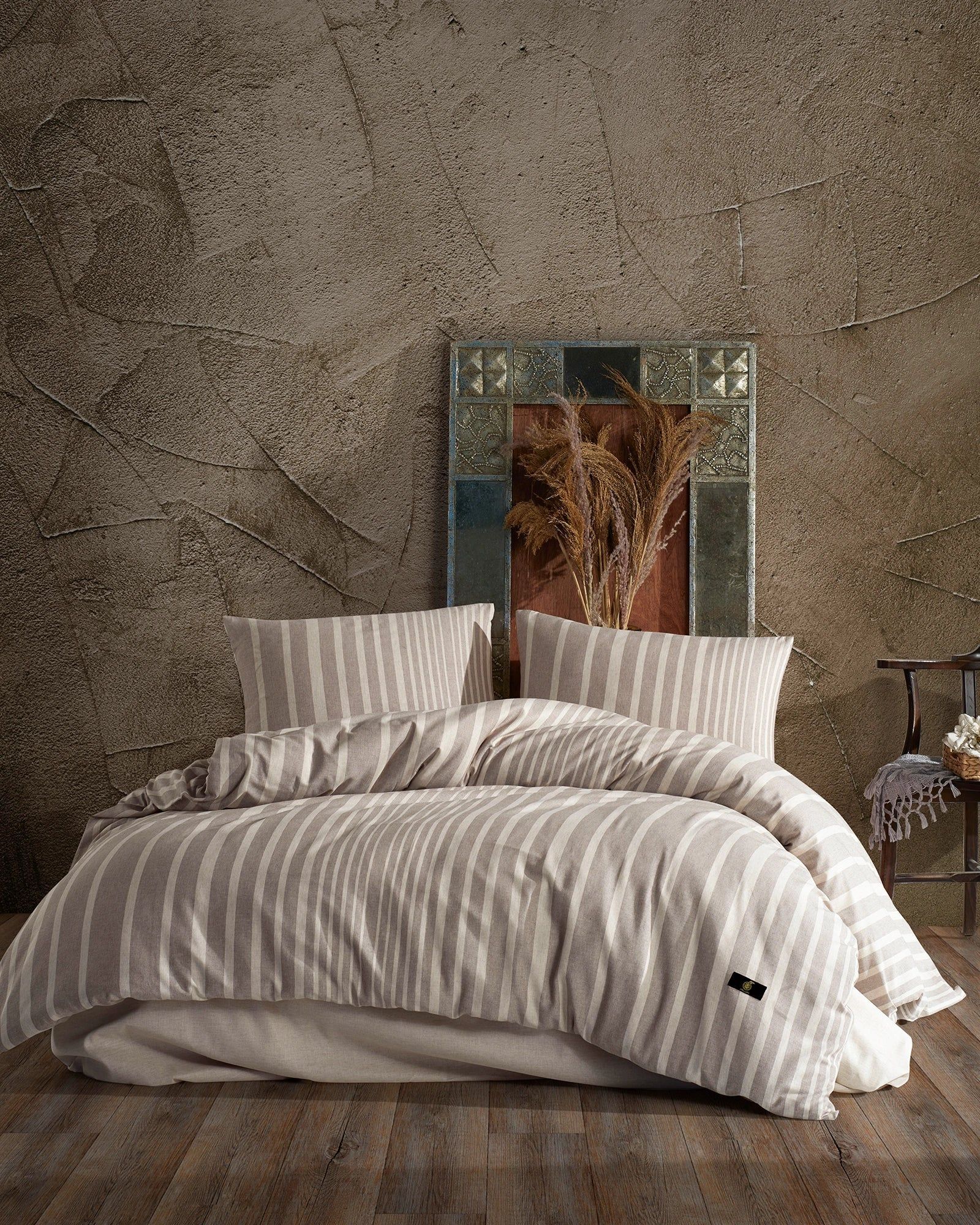 Cozy bed with striped bedding and pillows against a textured brown wall with a framed abstract artwork above.