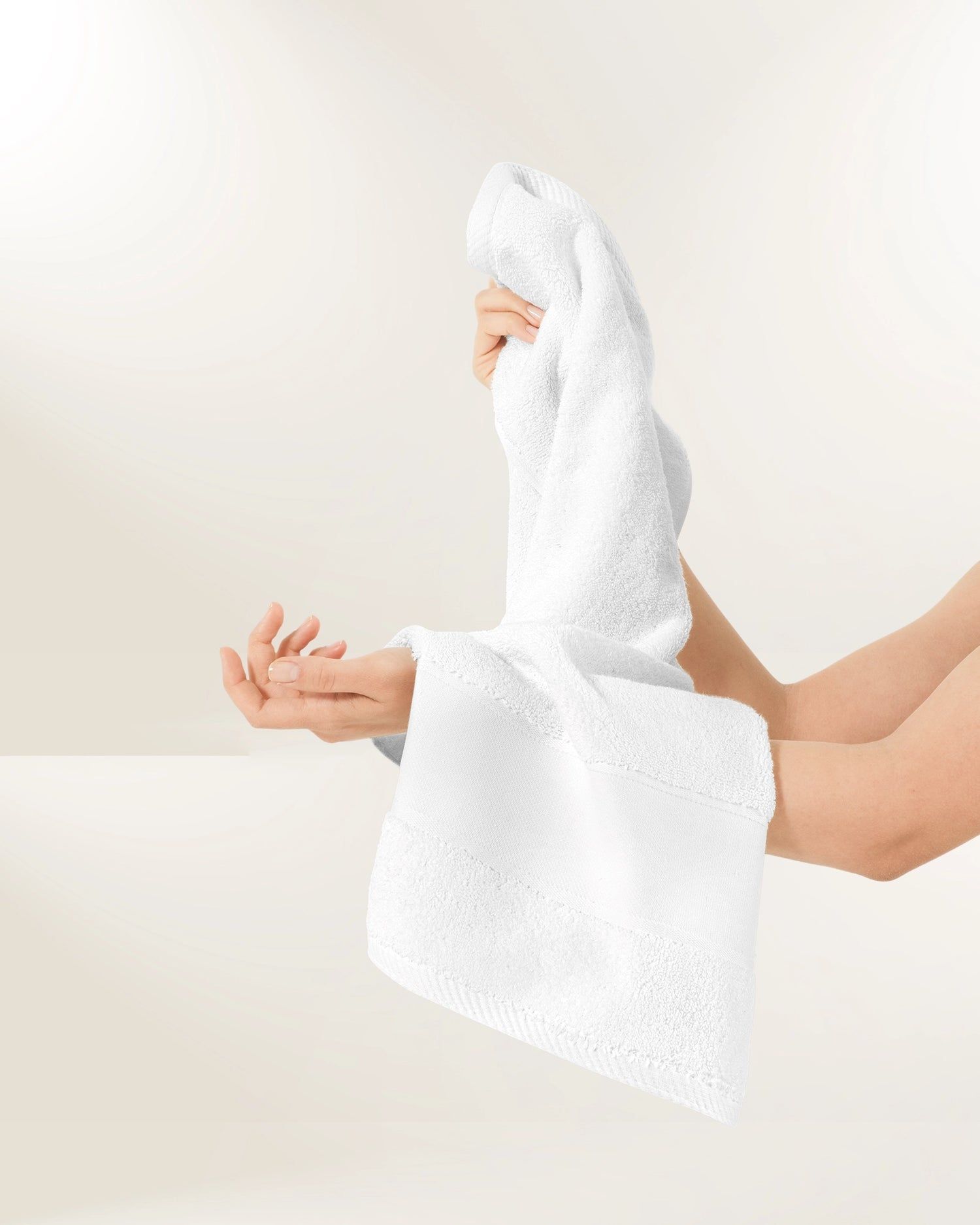 Baby wrapped in a white towel, held in hands against a light background