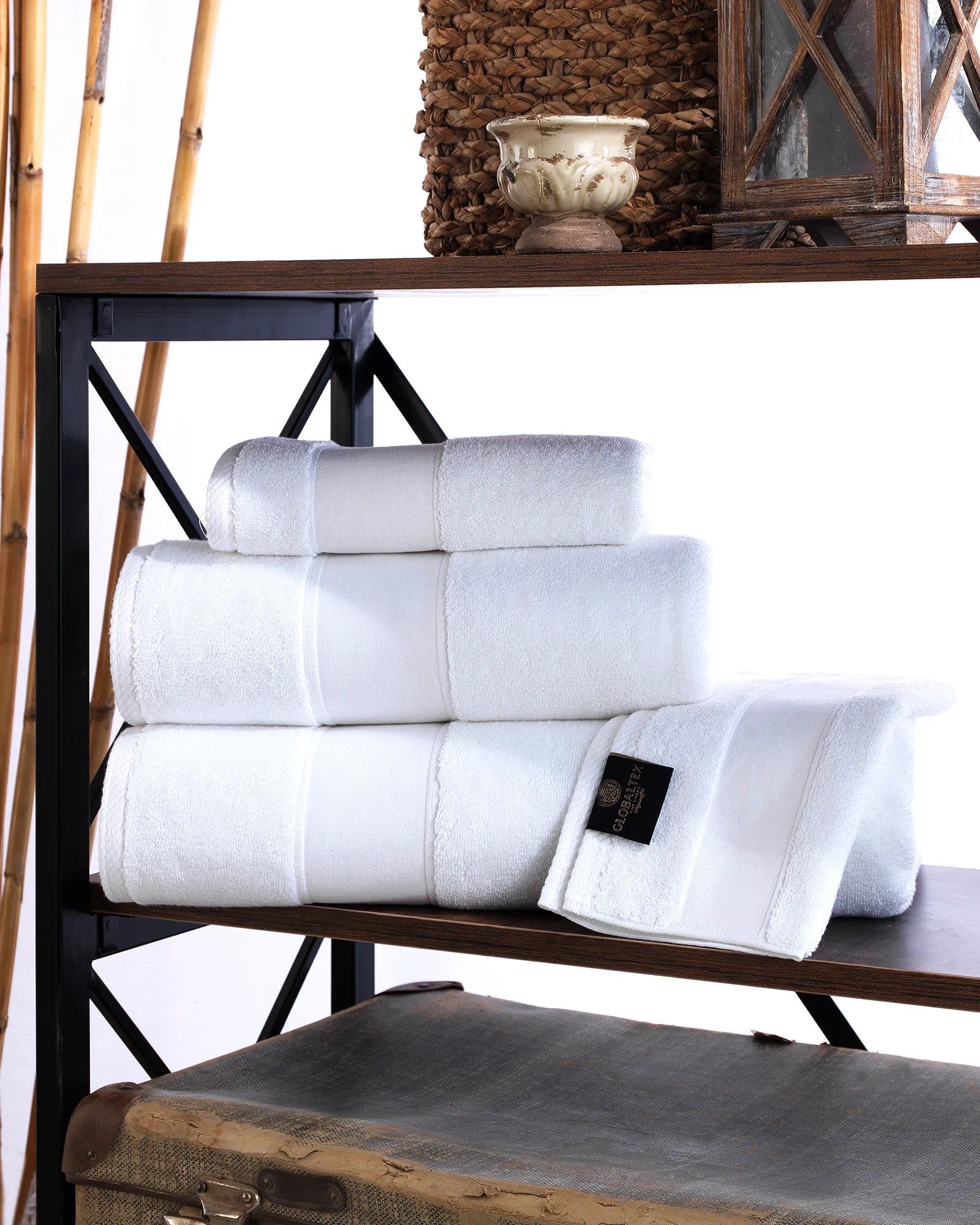 Stacked white towels on a black metal shelf with a woven basket and decor accents