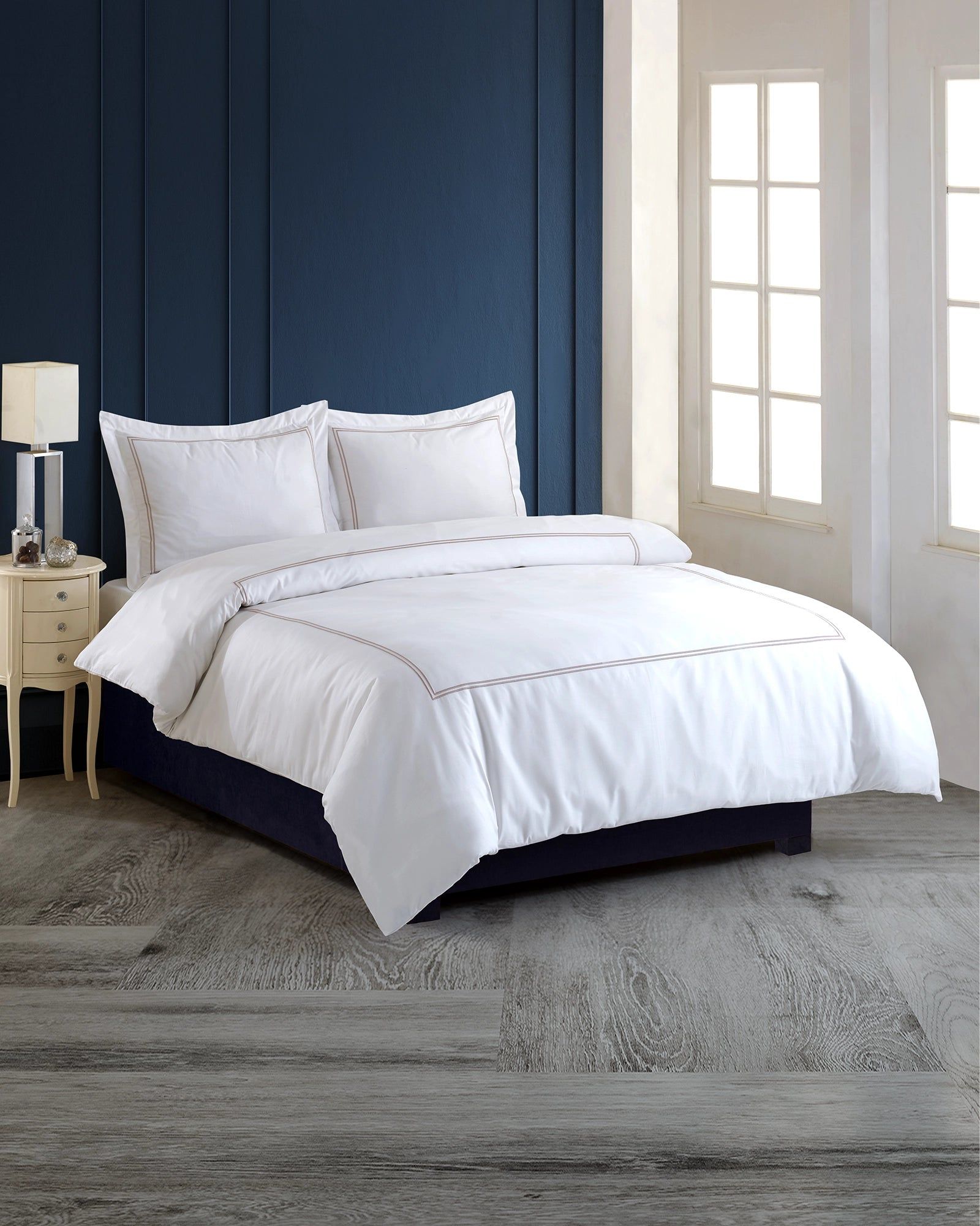 White bed with pillows and duvet in a bedroom with a navy blue upholstered headboard and gray rug