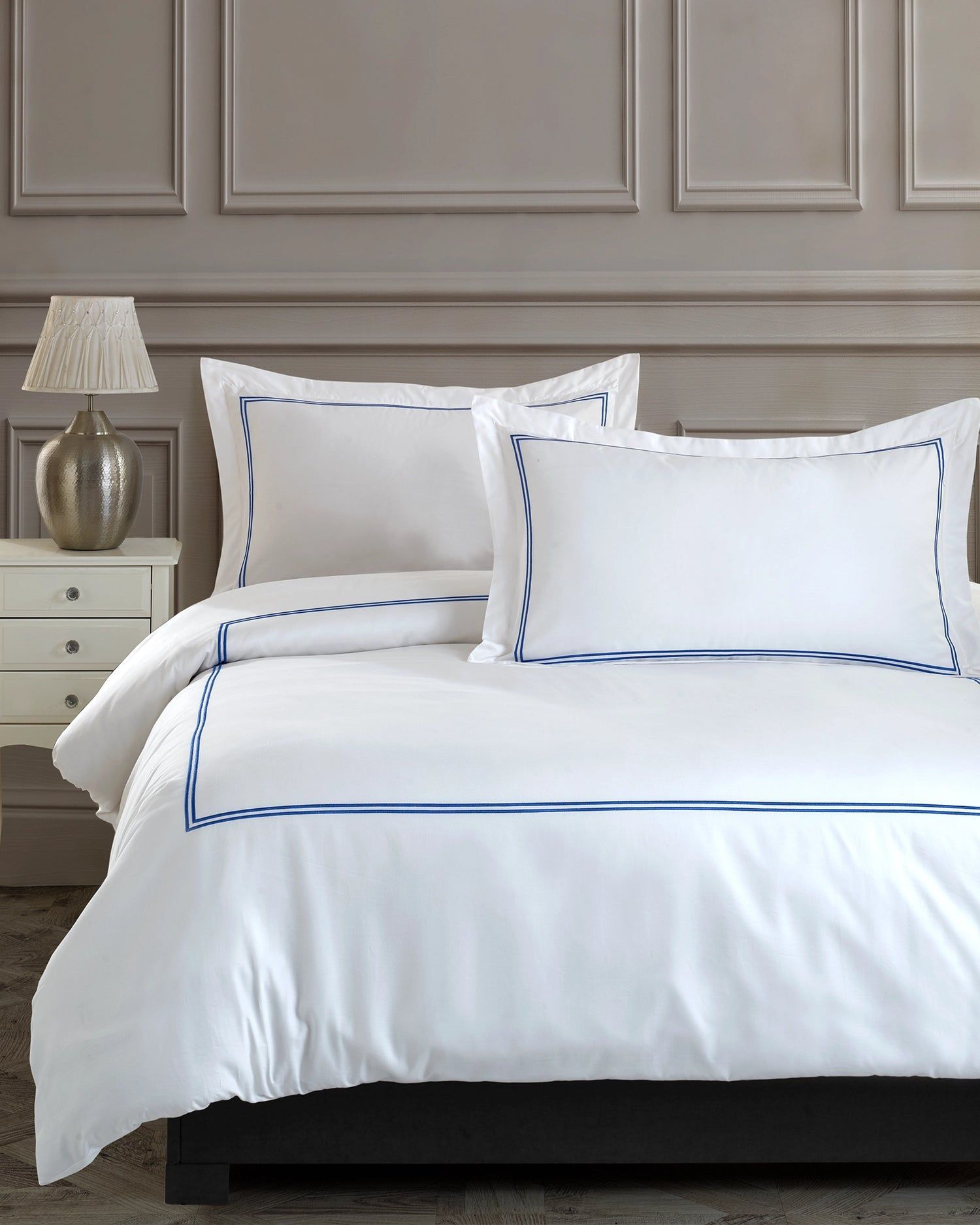 White bed with blue-trimmed bedding and pillows in a gray-paneled bedroom