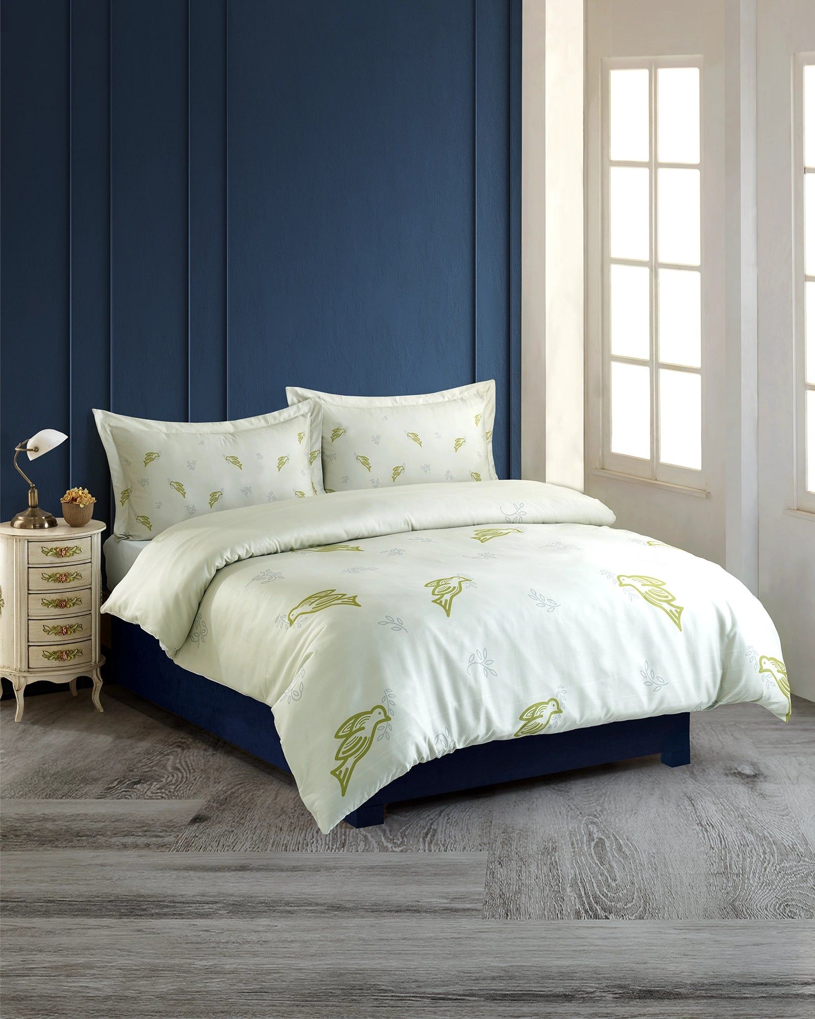 Blue bedroom with a white floral bedspread, matching pillows, and a small bedside table by the window