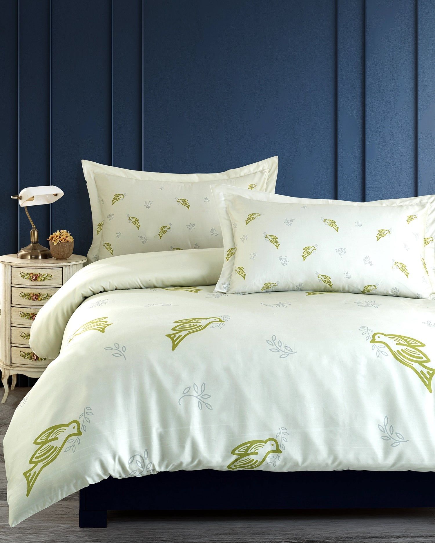 White floral bedding on a bed against a navy paneled wall, with a bedside table and lamp.