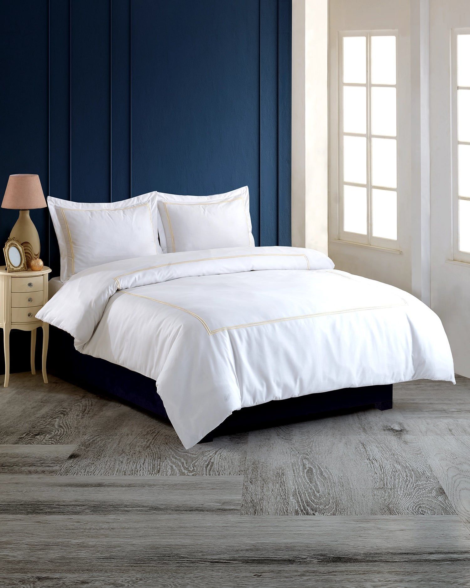 White bed with navy headboard in a bright bedroom beside tall windows, on a gray rug.