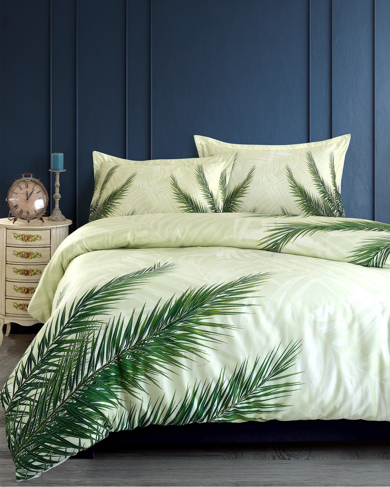 Green leaf-patterned bedding on a bed with blue paneled walls and a bedside table.