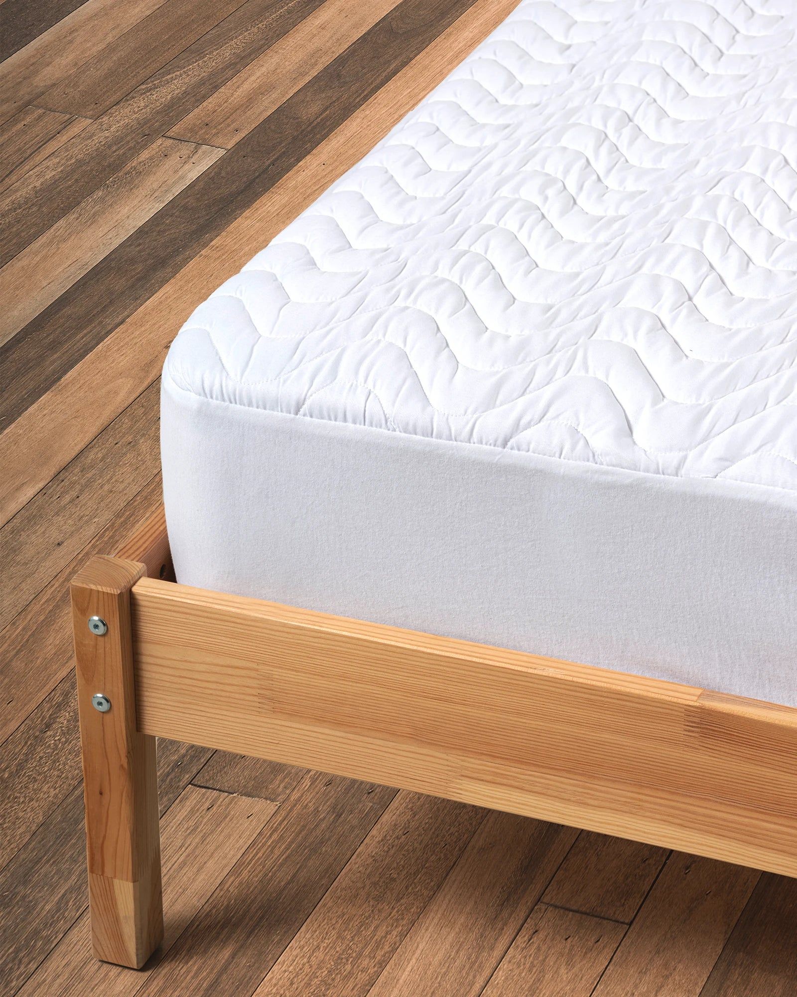 Wooden bed frame with white quilted mattress on a patterned rug