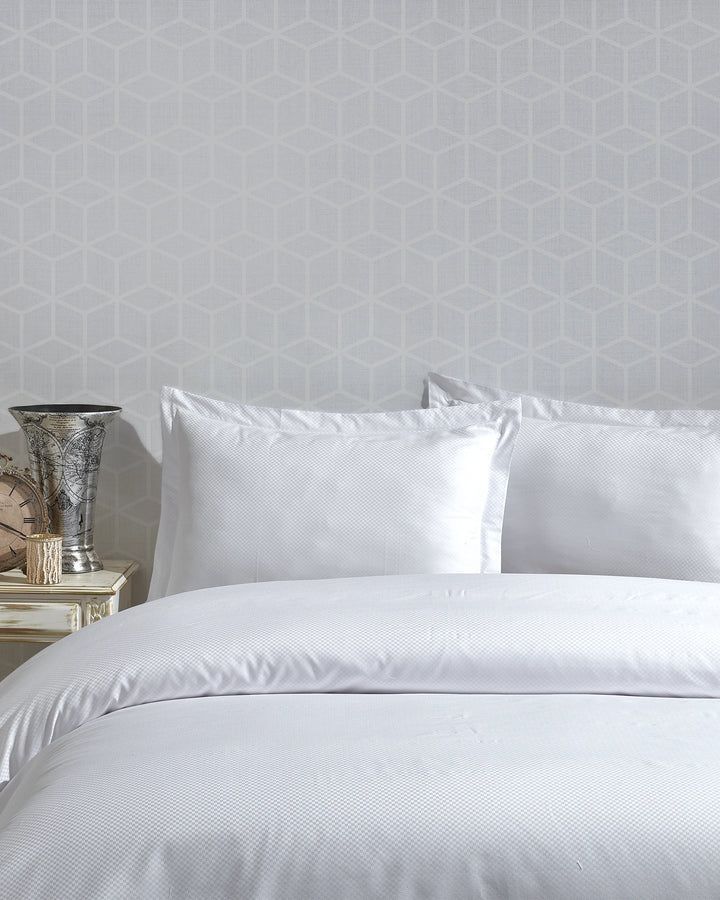 White bed with pillows and textured bedding against a light gray patterned wall.