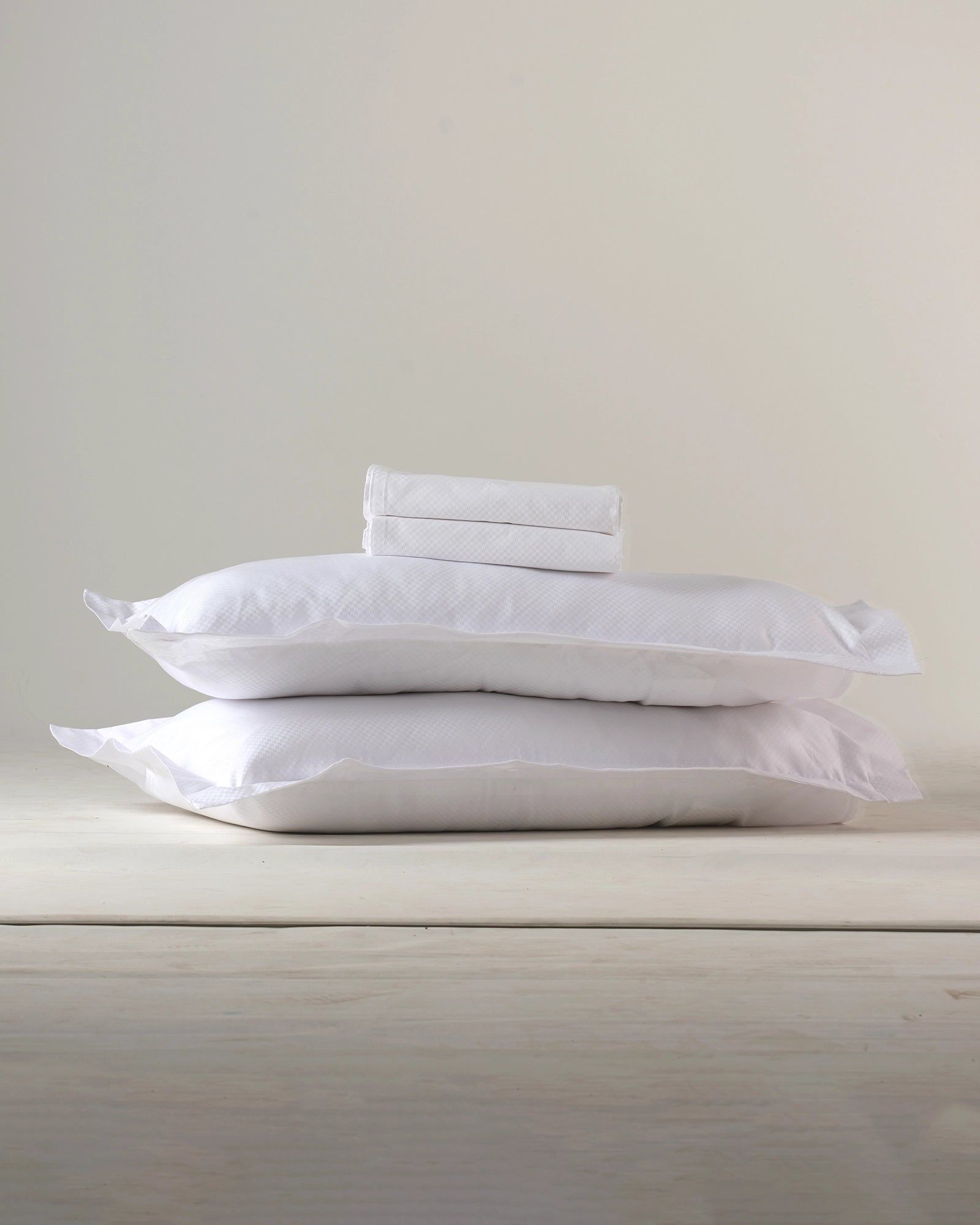 Two white stacked pillows or folded towels on a light wooden surface against a beige wall