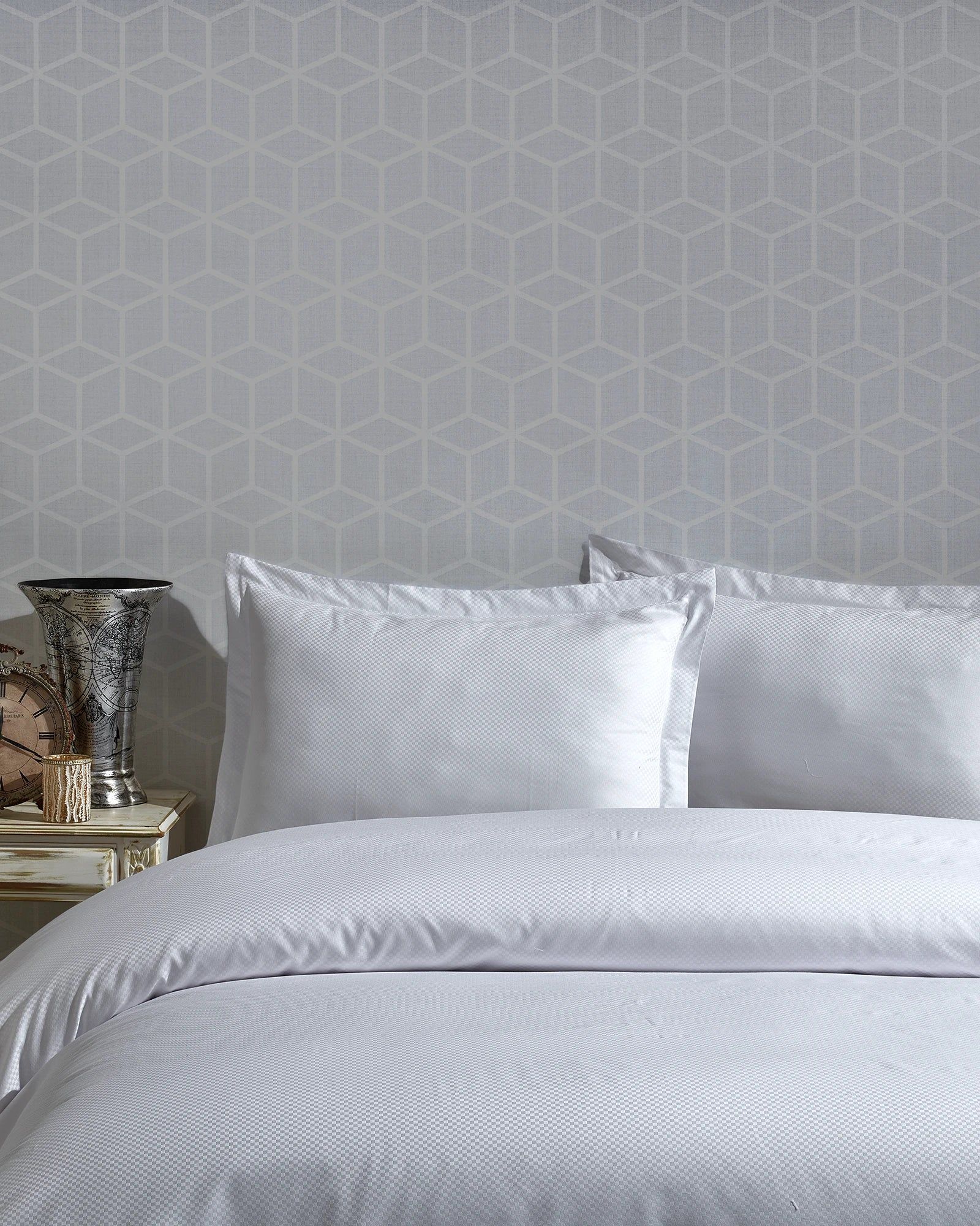 White bed with pillows and textured wallpaper in a softly lit bedroom