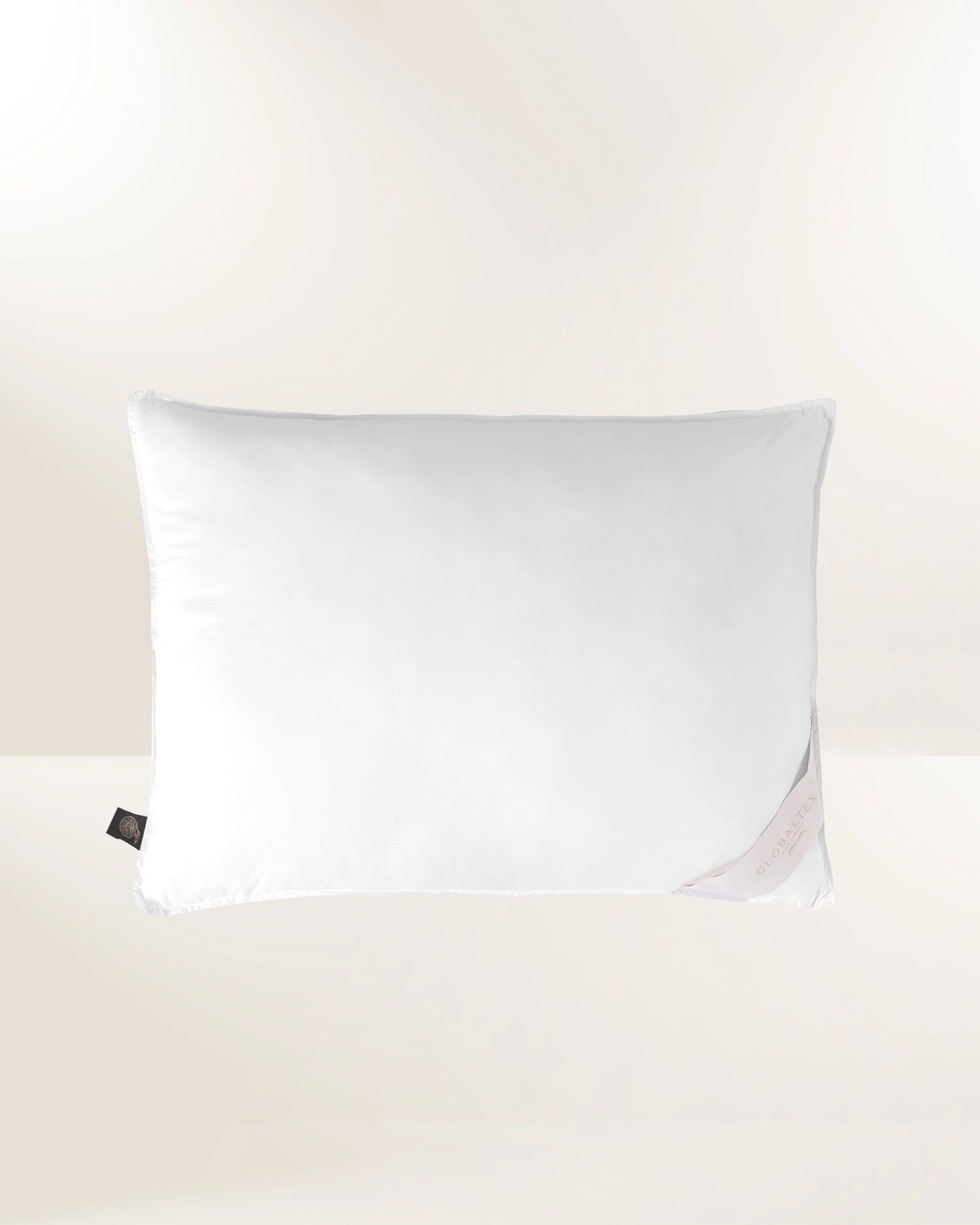 White pillow on a light beige background, with a small corner tag visible