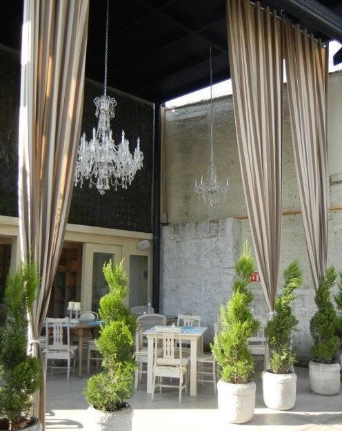 Outdoor patio with white chairs, hanging drapes, crystal chandeliers, and potted shrubs in front of a café