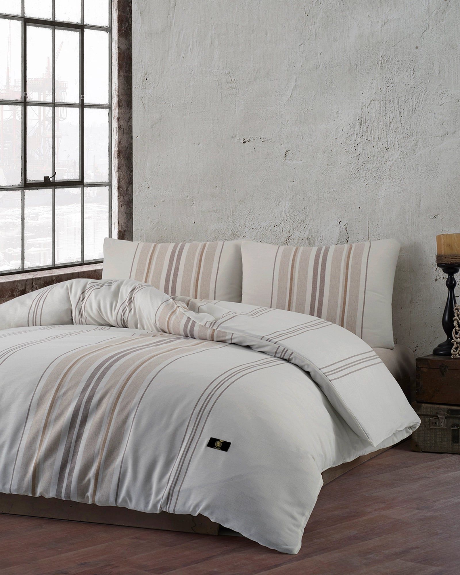 Neutral-toned bed with striped pillows and bedding in a minimalist bedroom by a large window