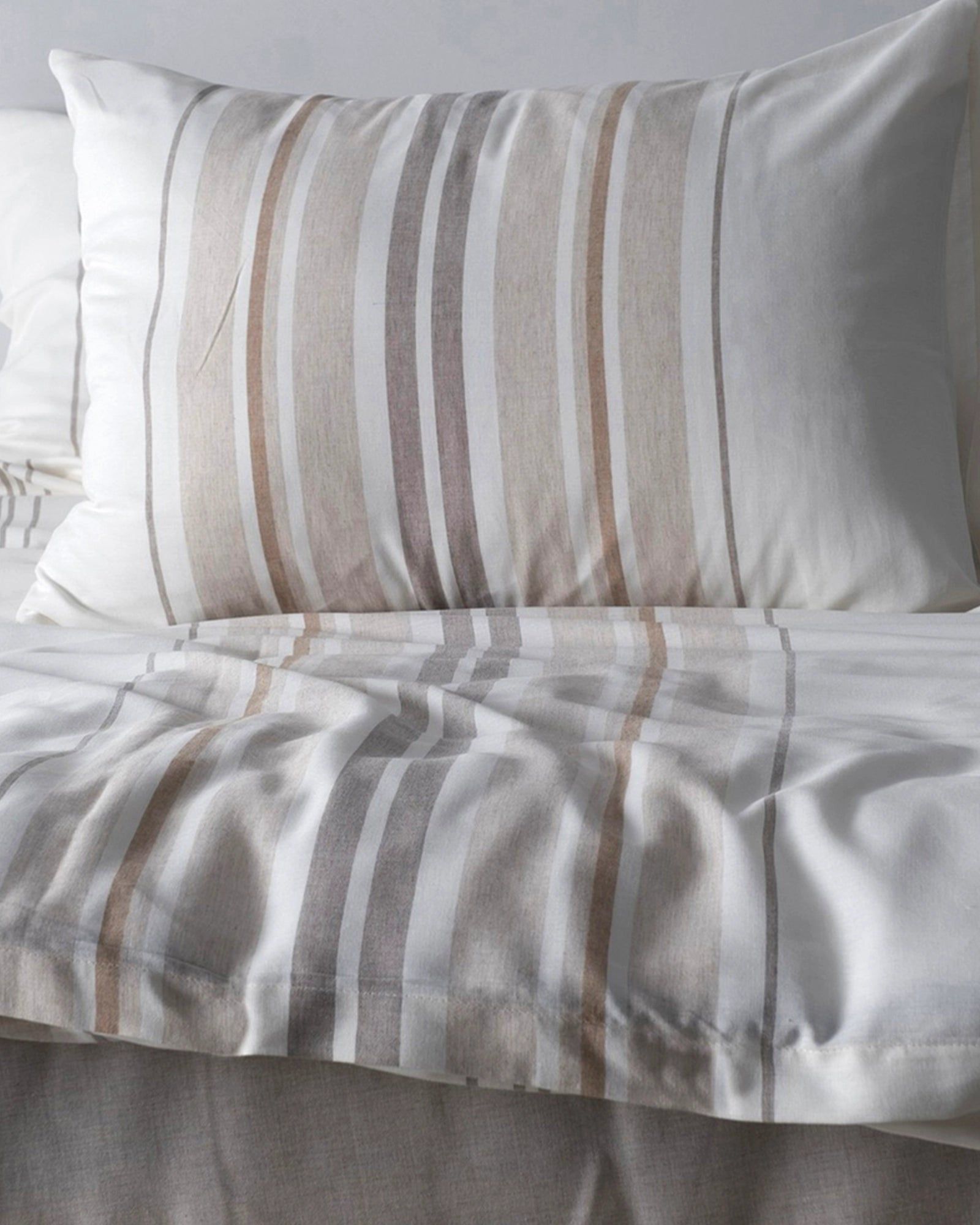 Neutral striped beige and gray bedspread with matching pillow on a bed