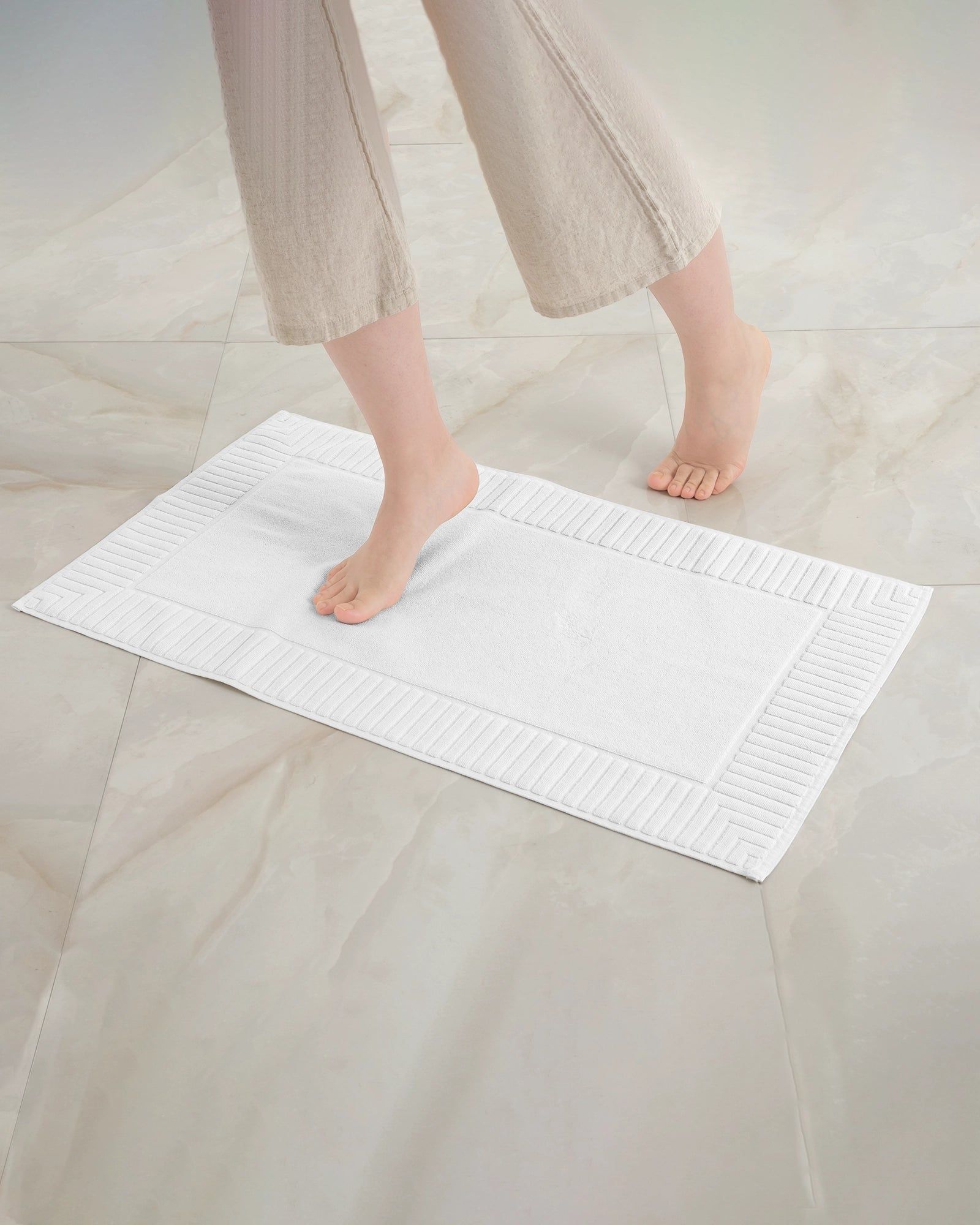 Feet standing on a white textured mat on a light tiled floor.