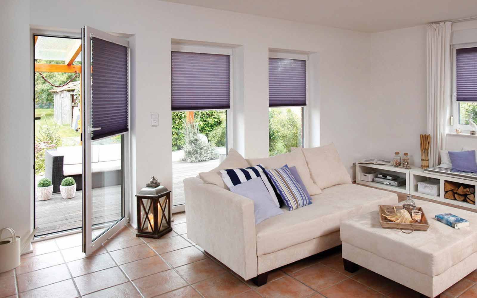 Bright modern living room with white sofa, ottoman, tiled floor, and open doors to a patio.