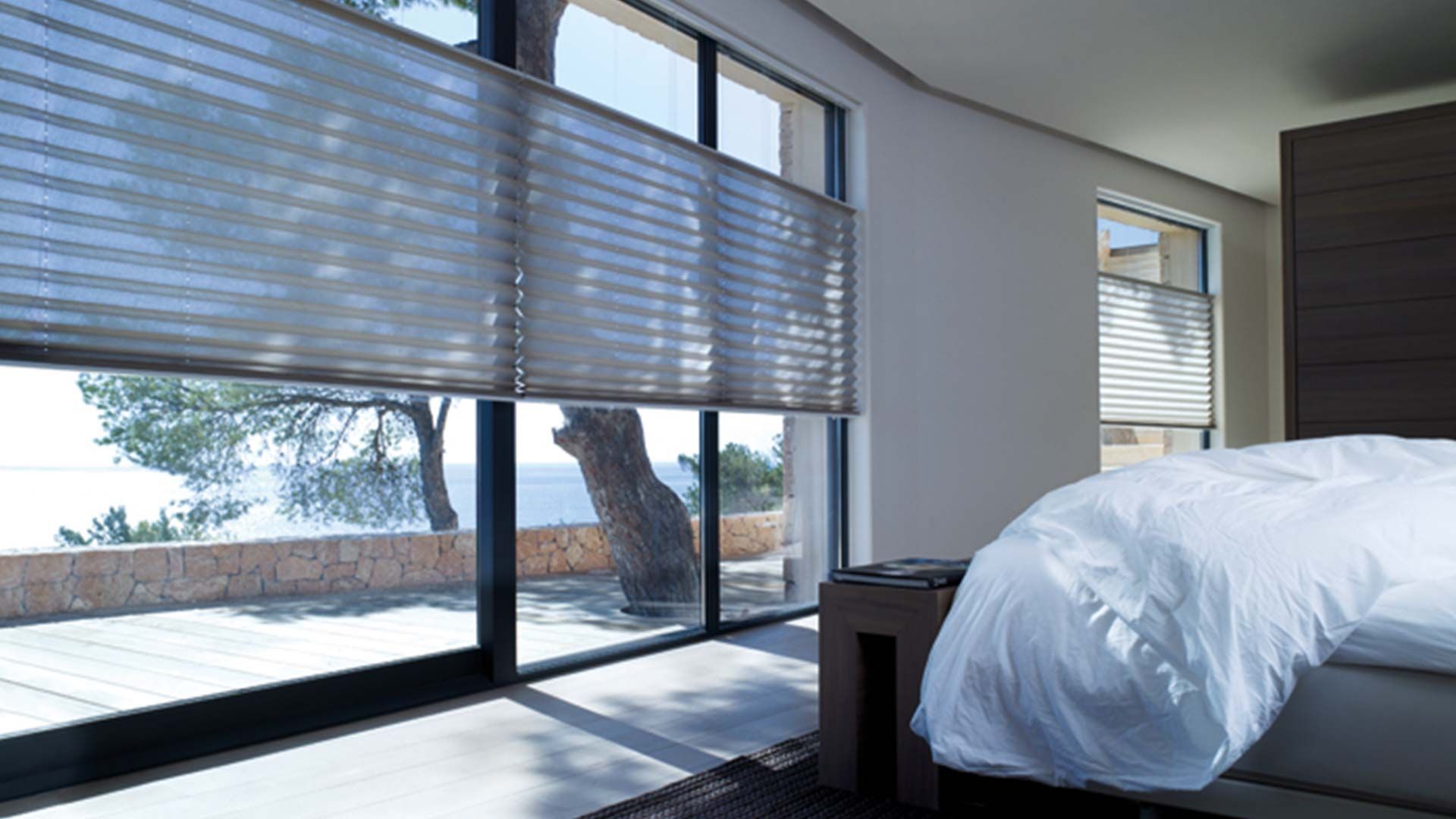 Modern bedroom with large windows, blinds, bed, and ocean view