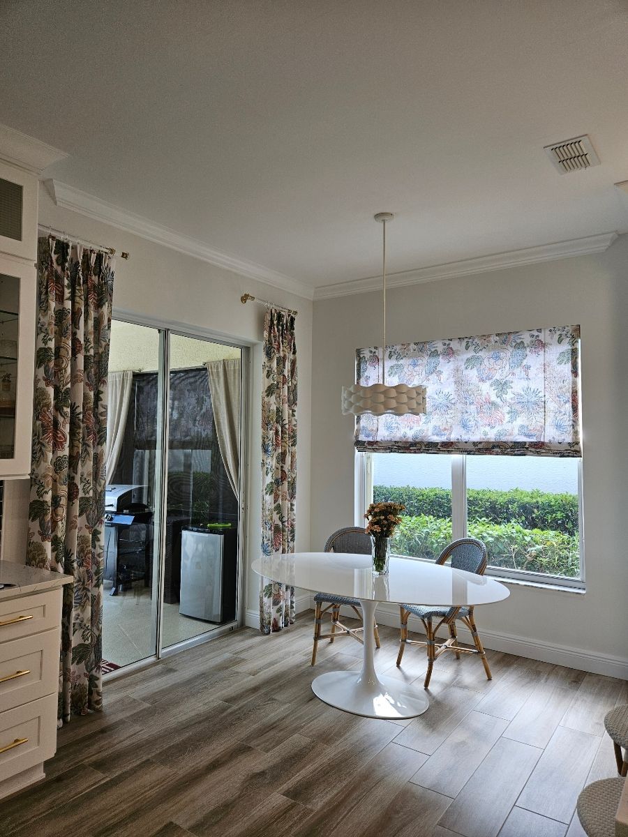 Bright dining nook with white table and chairs, wood floors, and large windows with curtains.