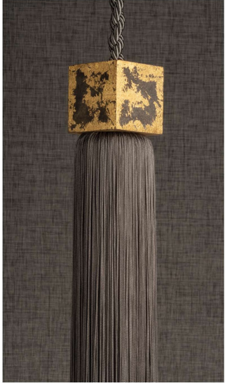 Gold-and-black tassel or wall hanging with a long gray fringe on a dark textured background