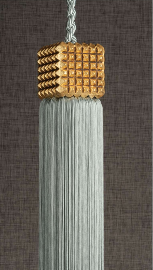 White tassel with gold woven top and braided cord hanging against a dark gray background
