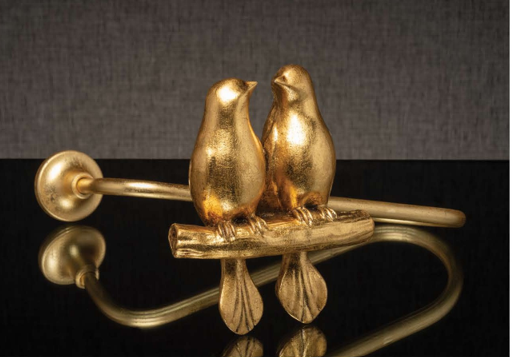 Two gold bird figurines perched on a brass rod against a dark background.