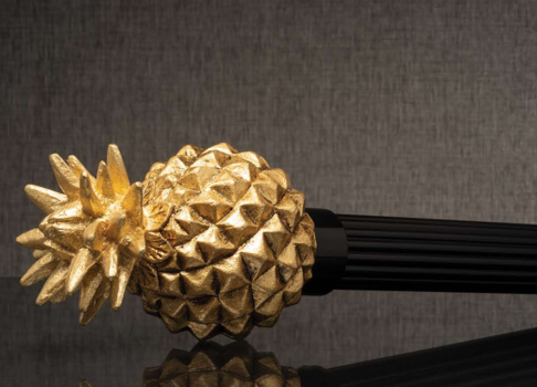 Gold pineapple-shaped decorative object with a pointed crown on a dark reflective surface