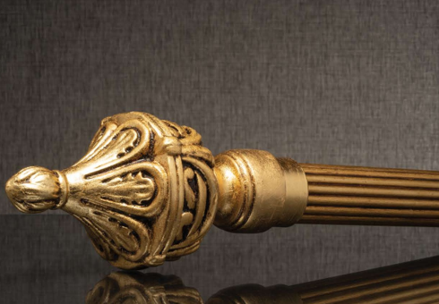 Gold ornamental finial on a decorative rod against a dark fabric background