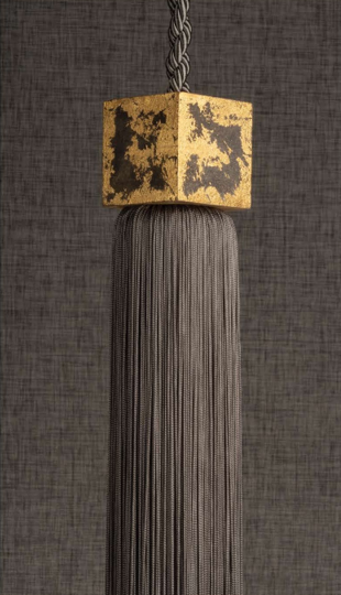 Gold and black decorative tassel hanging from a chain against a dark textured background