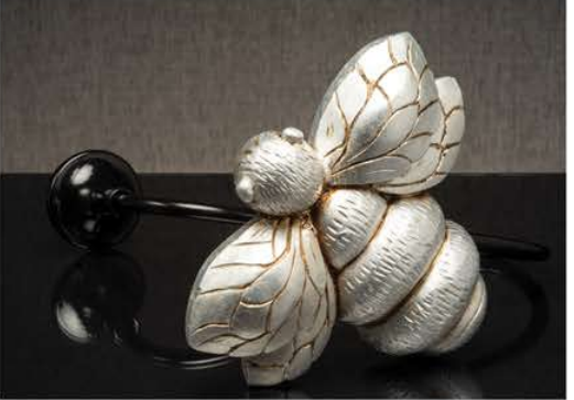 White flower hair accessory with gold-veined petals and black beads on a dark reflective surface
