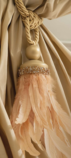 Beige decorative curtain tassel with braided cord and feathered fringe tied to draped fabric