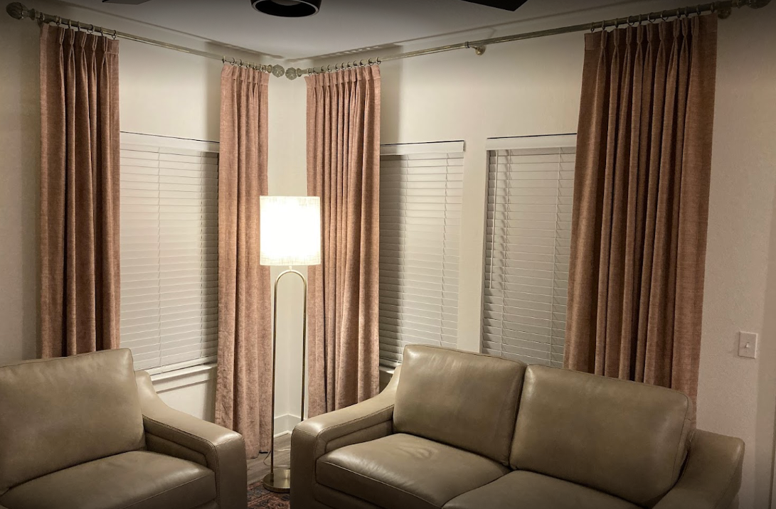 Living room corner with beige sofas, a floor lamp, and pink curtains by the windows