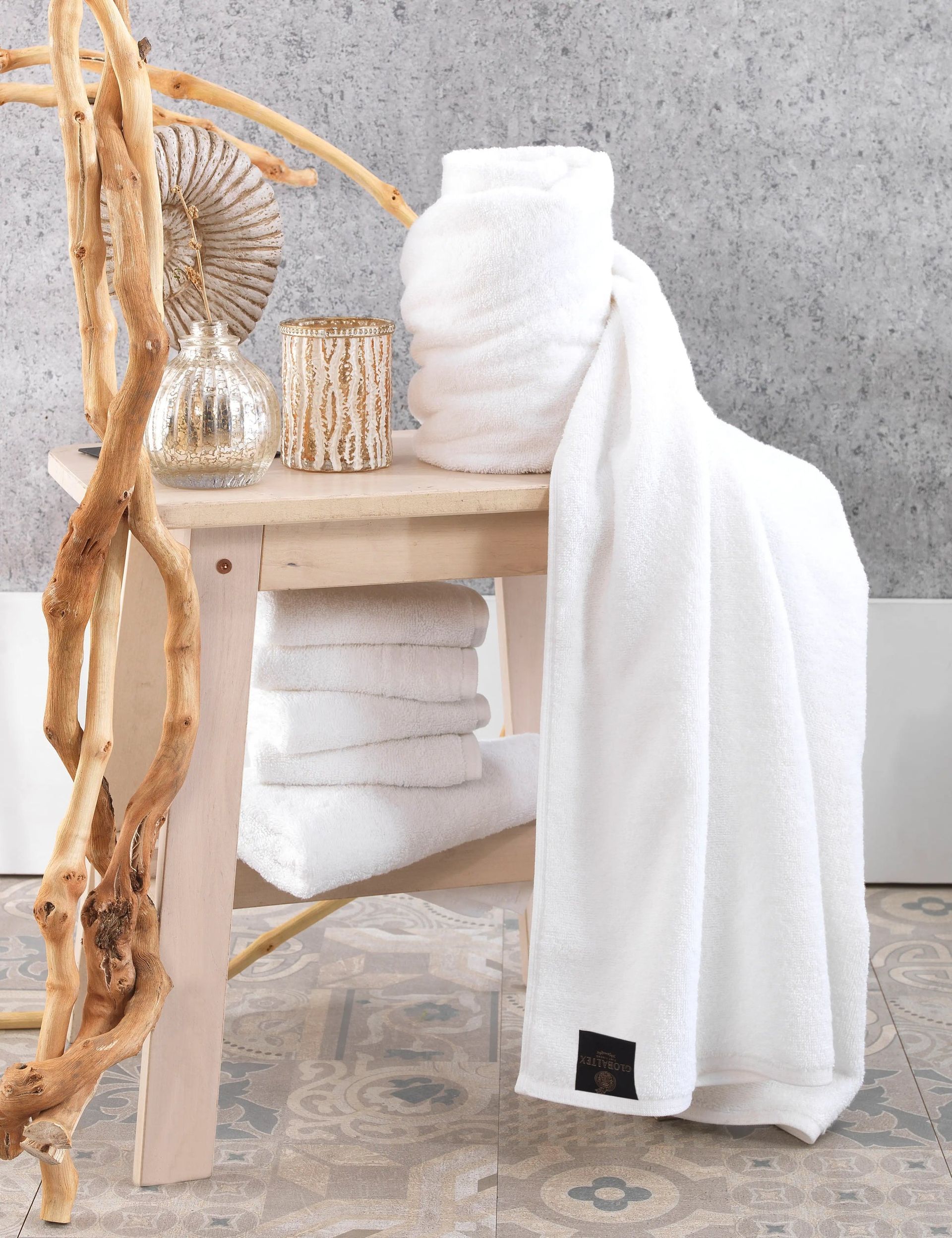 White towel draped over a light wood bench with woven baskets and a textured gray wall backdrop