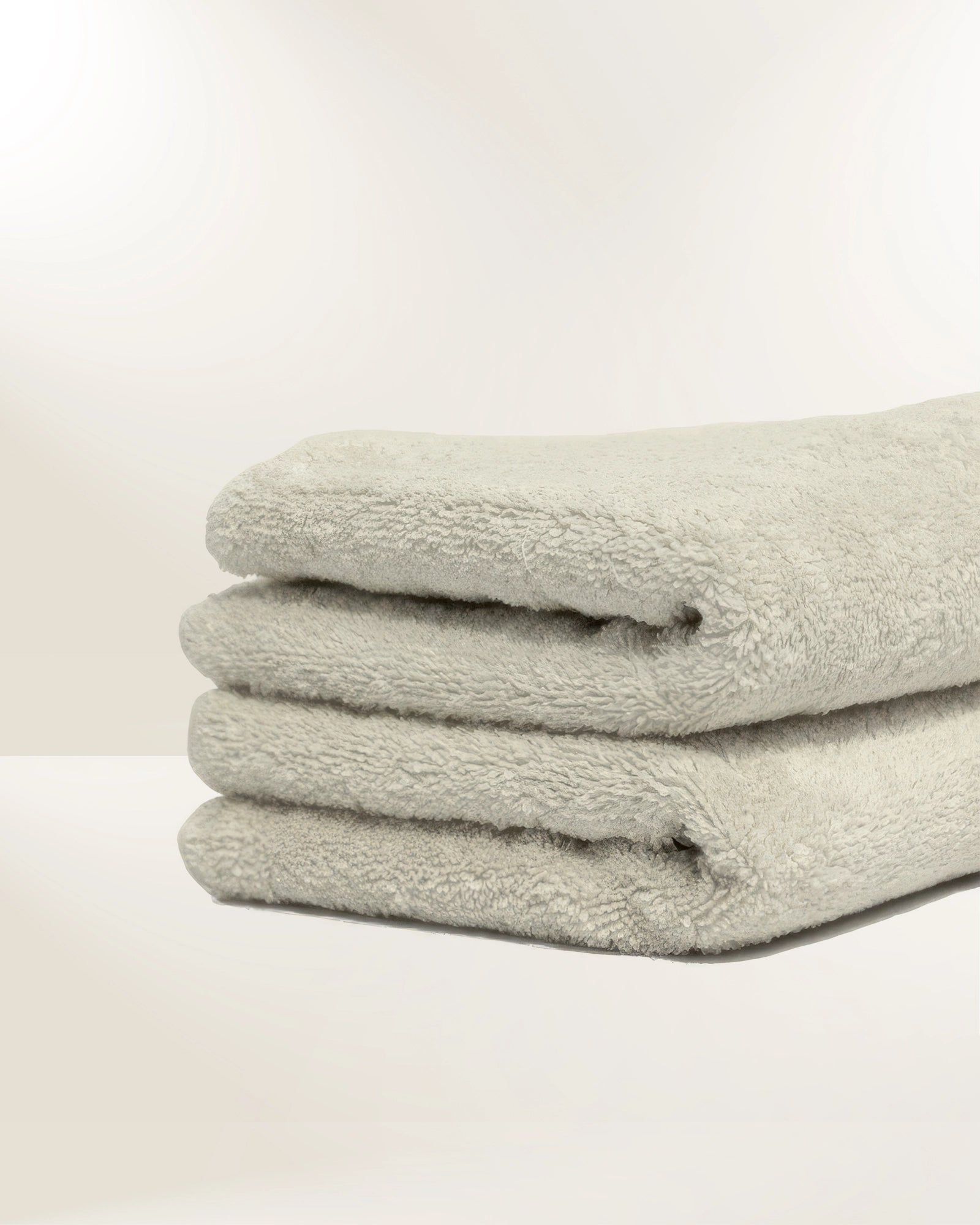 Three folded light gray towels stacked on a white surface against a plain background